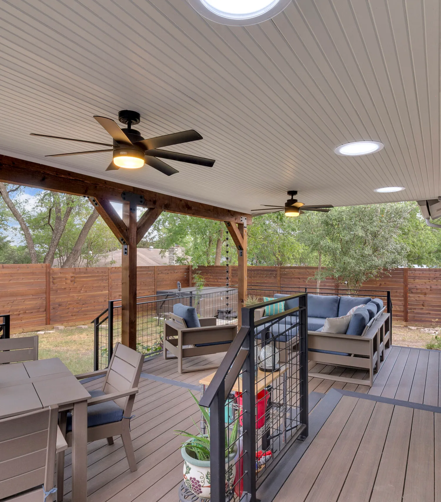 Covered patio with beadboard ceiling, dual ceiling fans, recessed lights, blue sectional sofa and cable railing