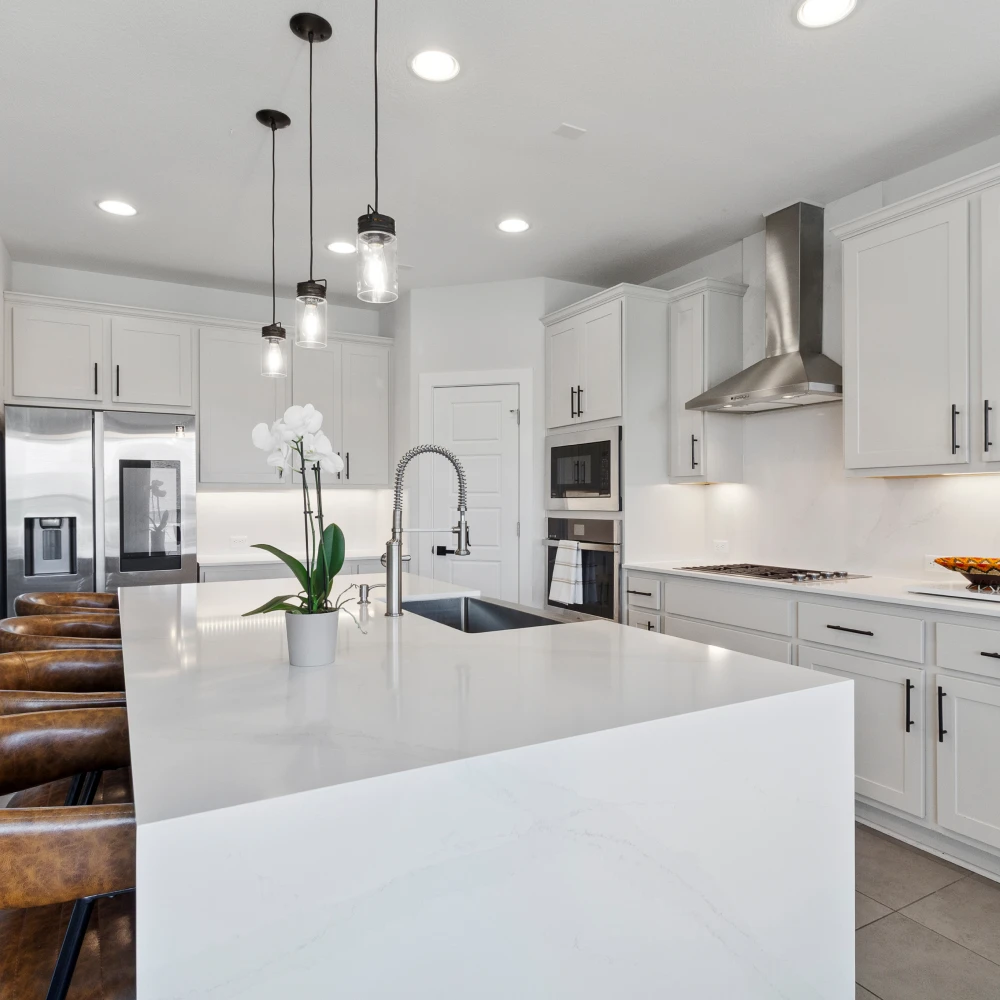Modern kitchen with marble island featuring brown leather stools, pendant lights, and stainless steel appliances.