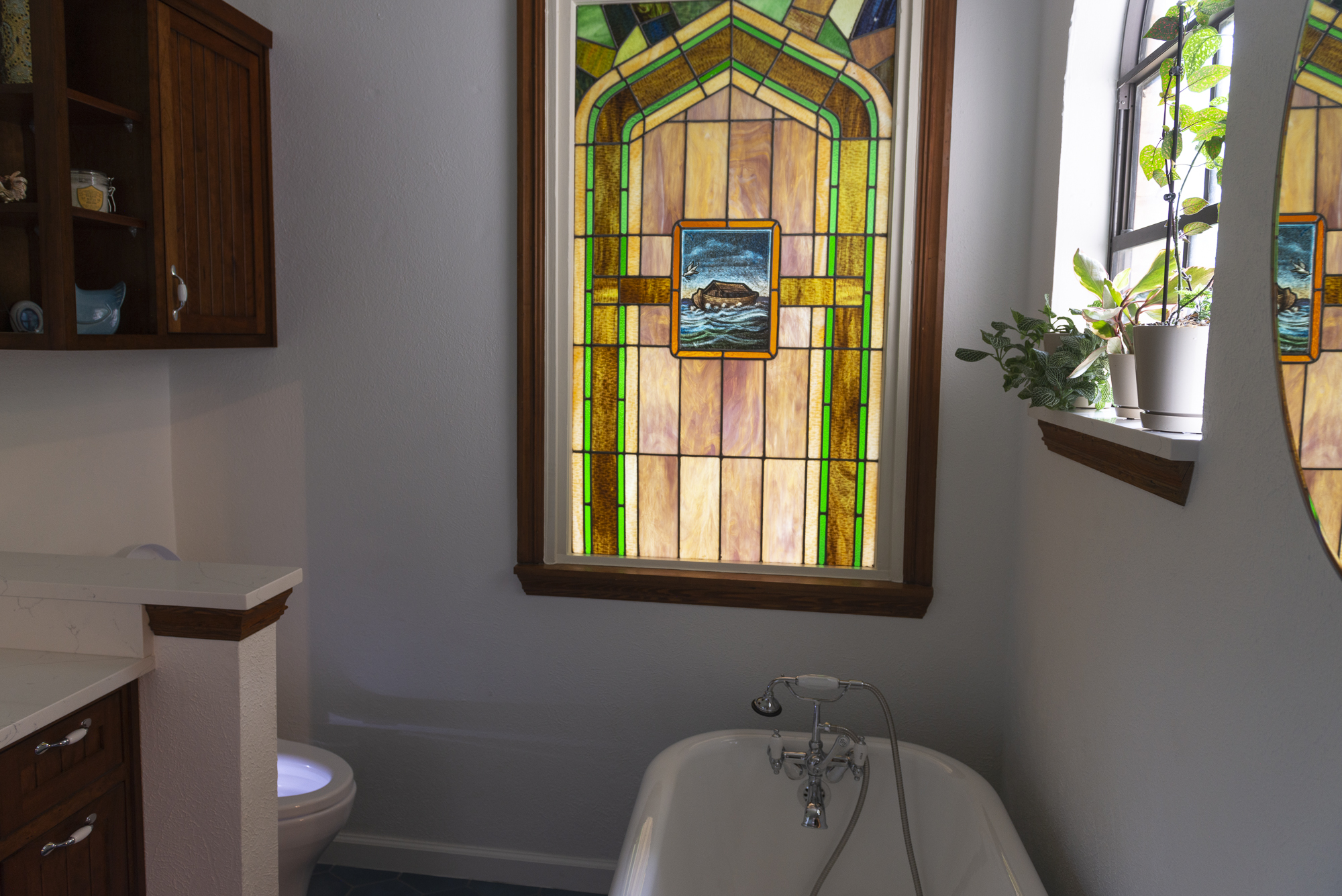 A bathroom featuring a stained glass window and a white toilet, creating a colorful and serene atmosphere. Bathroom renovation project in Buda, TX.
