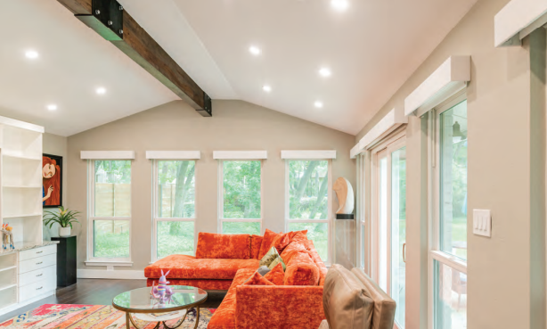 Bright living room with orange sectional sofa, wooden beam ceiling, and large windows overlooking greenery.  Dining and Living Room Renovation in Austin, TX.