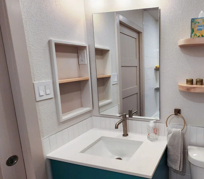 Modern bathroom vanity with white countertop, teal cabinet, recessed shelves, and large mirror above sink. Bathroom renovation in Austin, TX.