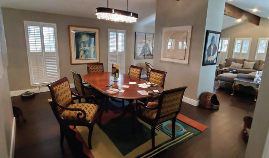Dining room with an oval wooden table, six patterned chairs, a modern chandelier, and framed artwork on beige walls. Before dining and living room renovation in Austin, TX.