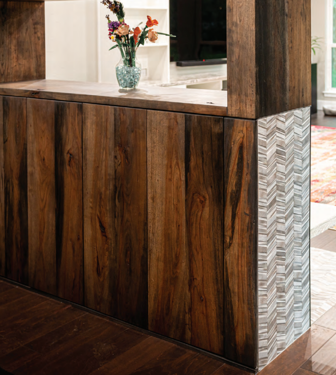 Modern wooden room divider with rich grain panels and a decorative chevron tile accent, topped with a glass vase of flowers. Dining and Living Room Renovation in Austin, TX.