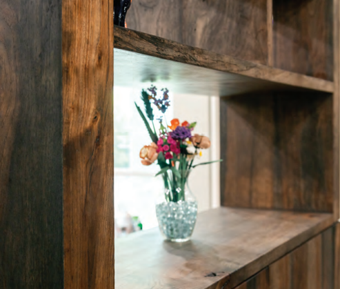 Wooden open shelving unit with a glass vase holding colorful flowers, positioned near a bright window. Dining and Living Room Renovation in Austin, TX.