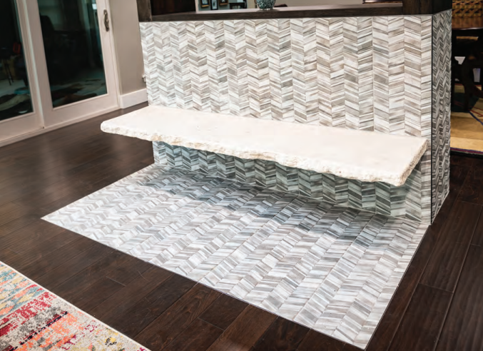 Floating stone bench with a natural edge mounted on a chevron-patterned tile wall and matching tile floor area in a modern interior. Dining and Living Room Renovation in Austin, TX.
