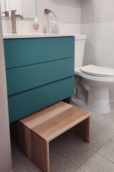 Bathroom with teal vanity, white sink, toilet, and wooden step stool on a tiled floor. Bathroom renovation in Austin, TX.